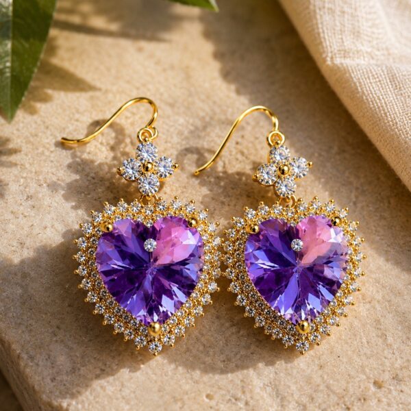 Pair of gold-plated purple heart drop earrings with clear cubic zirconia on a warm beige linen background — House of Ruhira