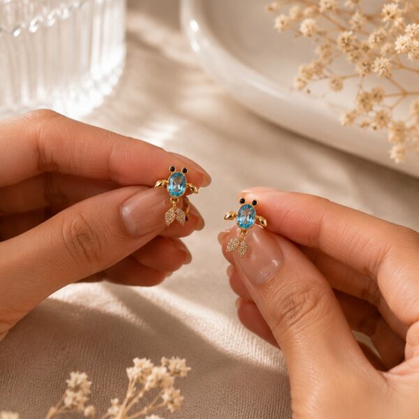 Pair of gold-toned blue crystal drop earrings with pave tails on a warm beige linen background — House of Ruhira