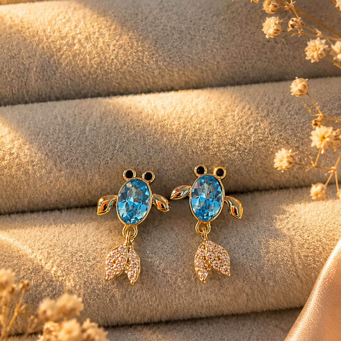 Flat lay styling of gold-toned blue crystal drop earrings with a silk scarf and a small clutch — House of Ruhira