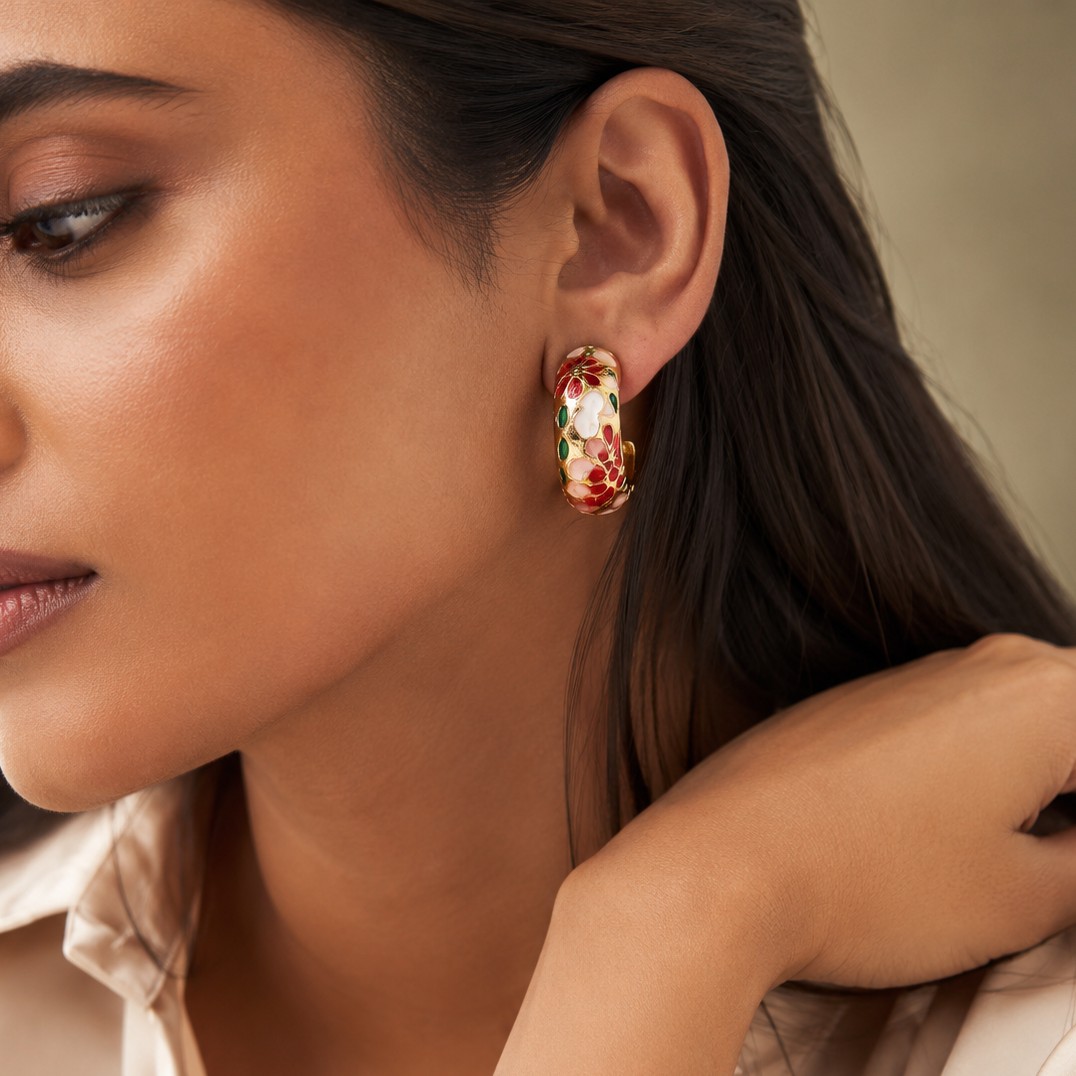 Model wearing gold-plated enamel hoop earrings with red, pink, white, and green floral design, showcasing them on her ear — House of Ruhira