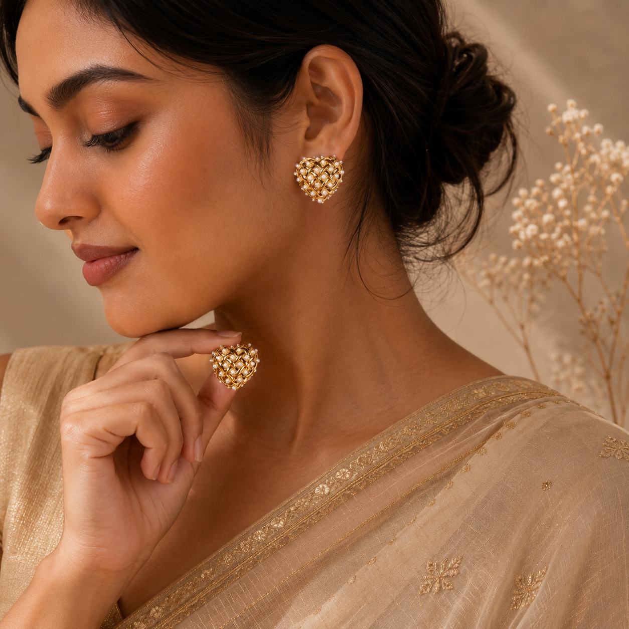 Model wearing gold-toned heart-shaped stud earrings with woven lattice and faux pearls on her ear — House of Ruhira