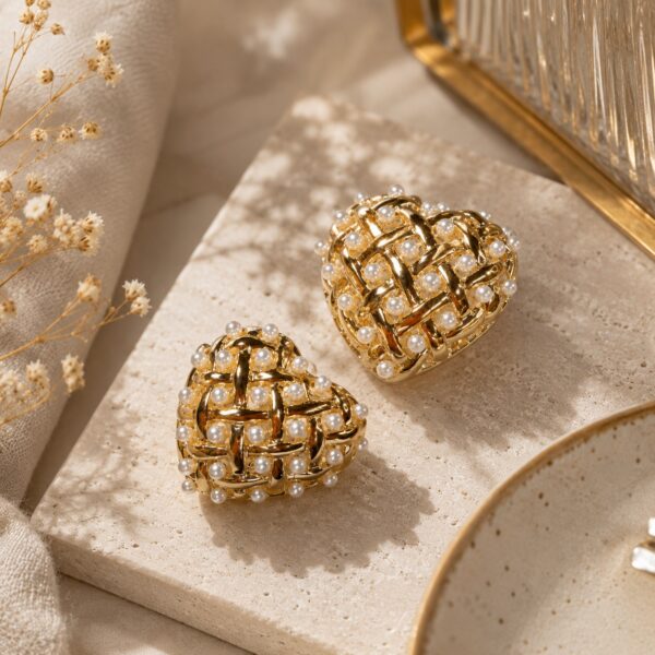 Gold-toned heart-shaped stud earrings with woven lattice and faux pearls on a clean white studio background — House of Ruhira