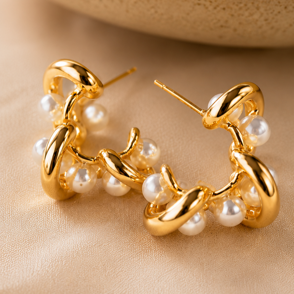 Flat lay styling of modern gold pearl drop earrings with a delicate gold chain and a small dried flower on a light neutral surface — House of Ruhira