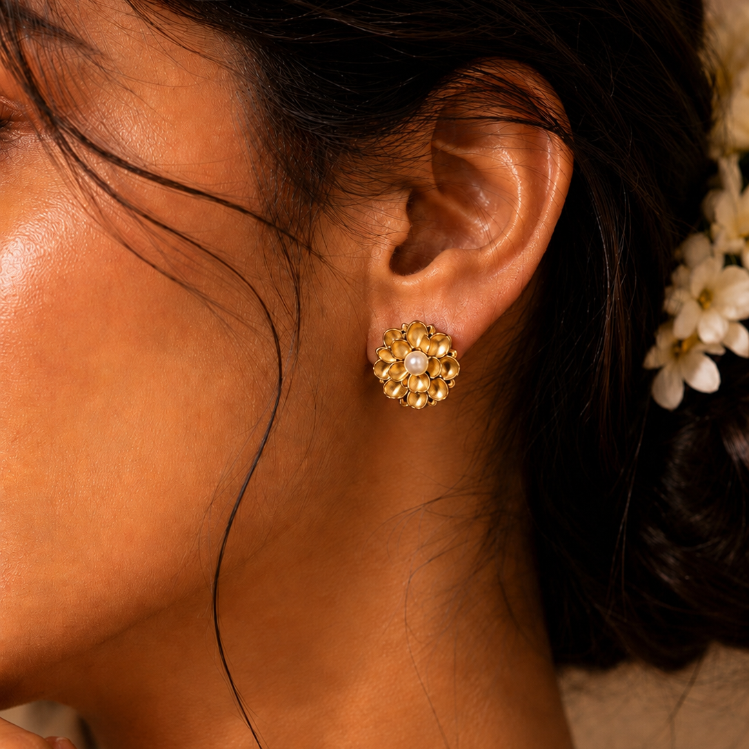 A model wearing textured gold floral stud earrings with central faux pearls, showcasing their elegant fit on the ear — House of Ruhira
