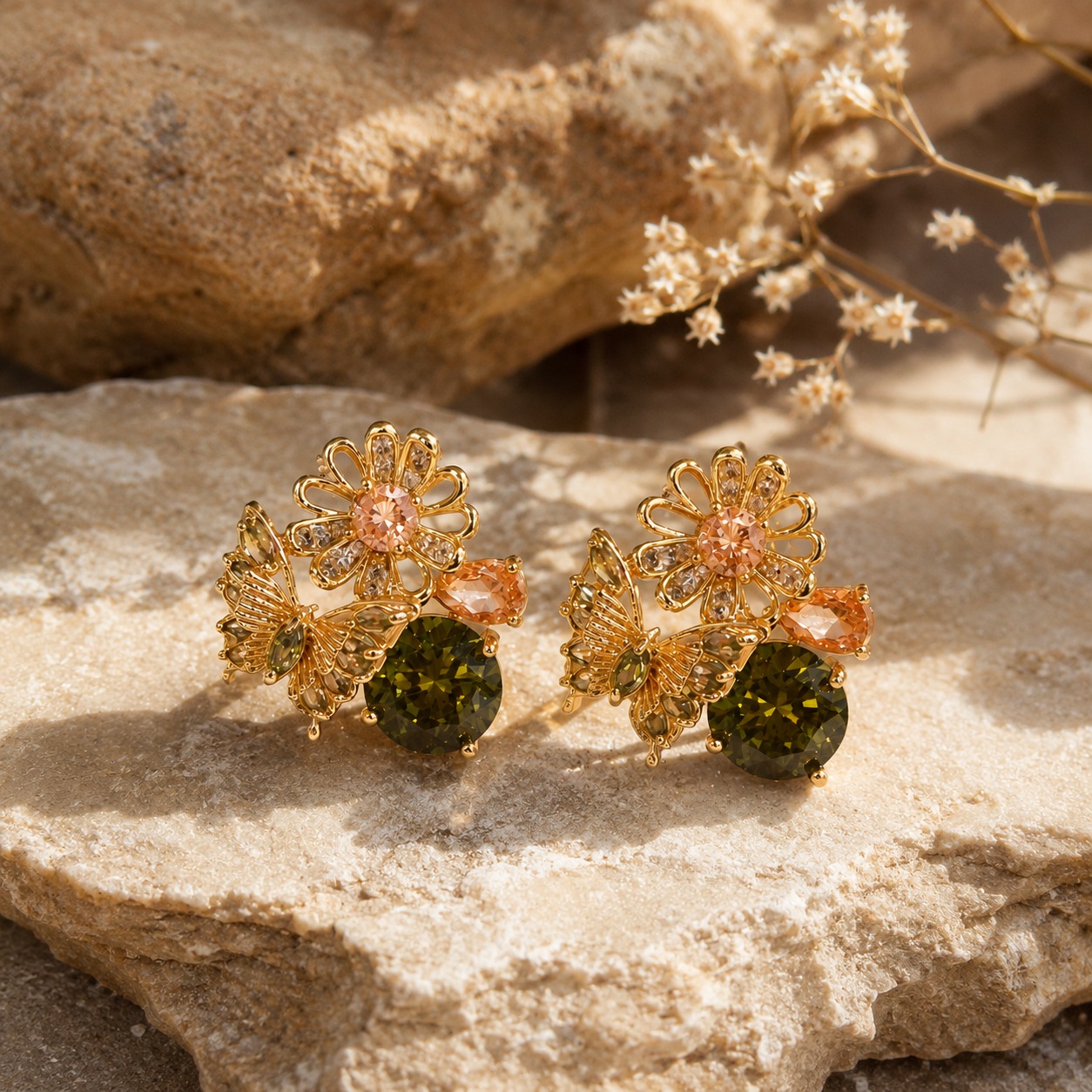 Gold-plated floral and butterfly stud earrings with olive green, peach, and clear cubic zirconia on a warm beige linen background — House of Ruhira