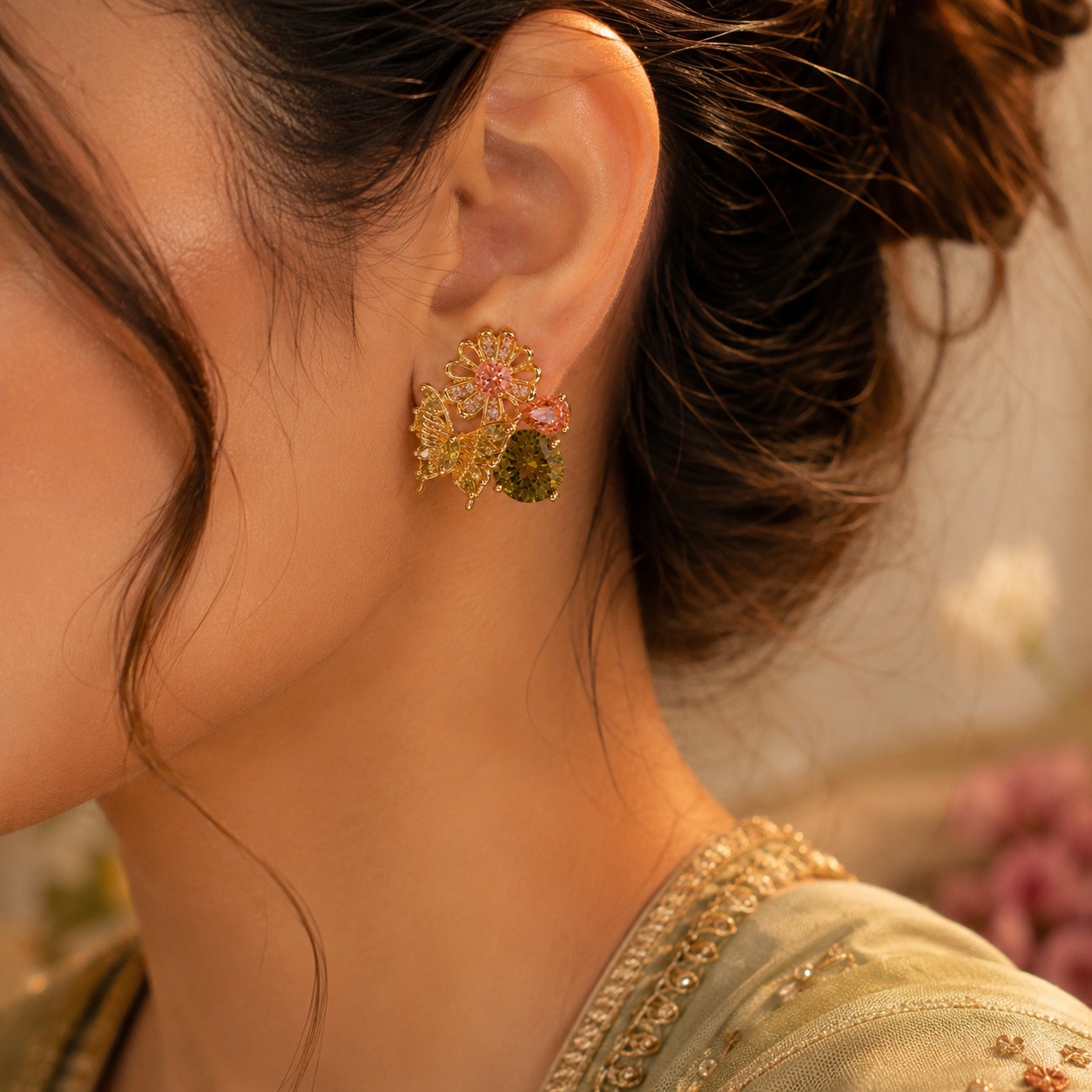 Model wearing gold-plated floral and butterfly stud earrings with olive green, peach, and clear cubic zirconia on her ear — House of Ruhira
