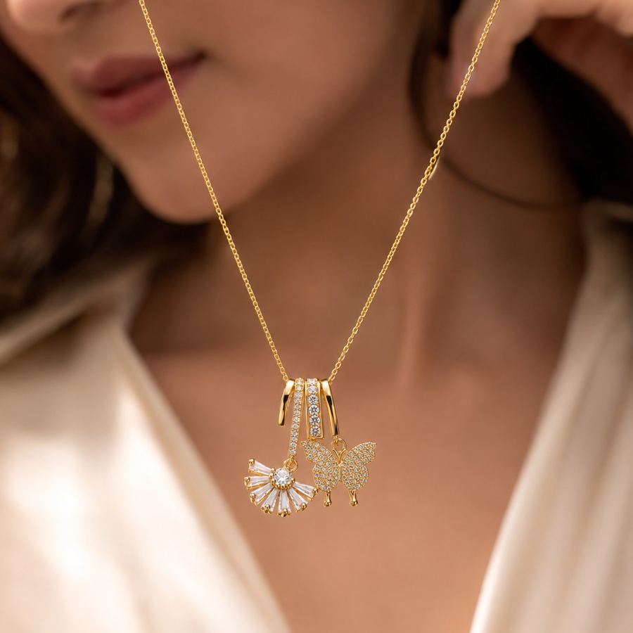 Flat lay styling of the gold charm necklace with butterfly and fan pendants, arranged with complementary accessories and soft fabric props – House of Ruhira