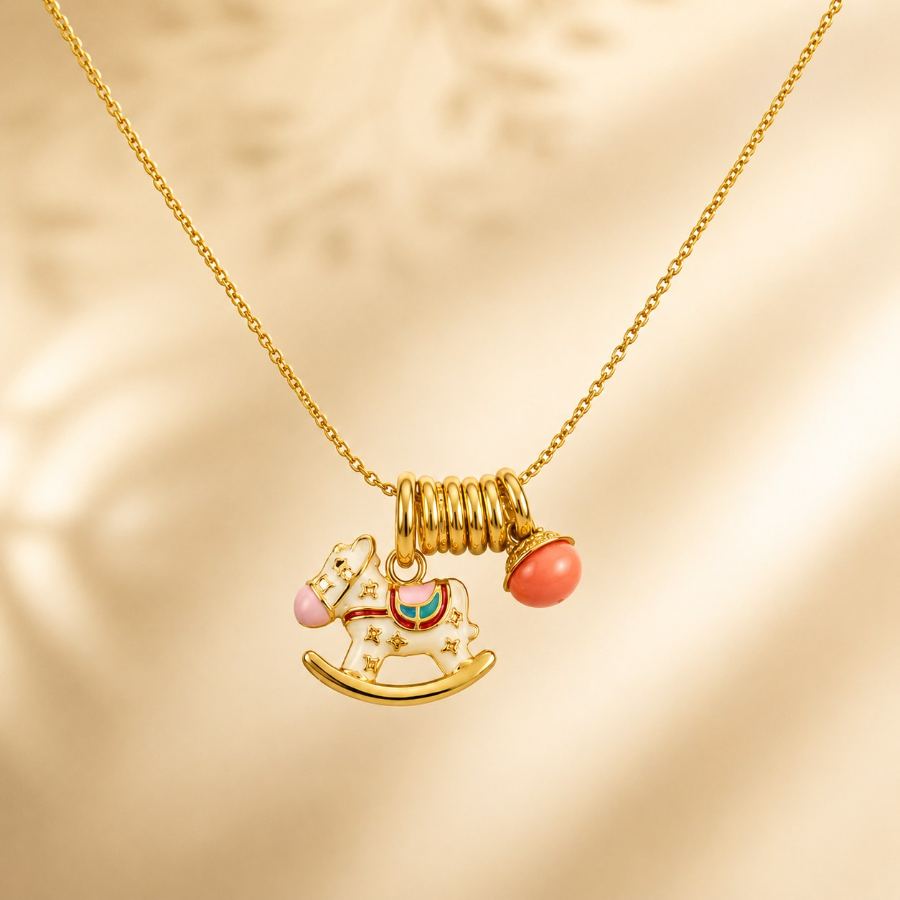 Flat lay styling of a gold-plated charm necklace with rocking horse and coral bell charms, styled with small dried flowers and a soft fabric – House of Ruhira